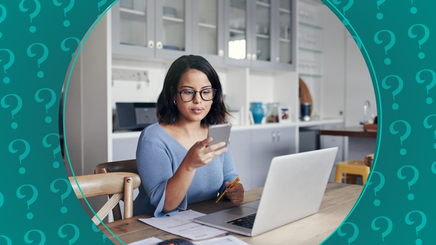 Woman looks at phone while working on a laptop