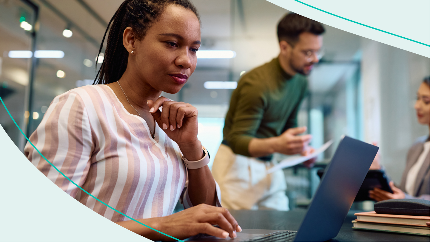 Woman works at her laptop with coworkers in the background