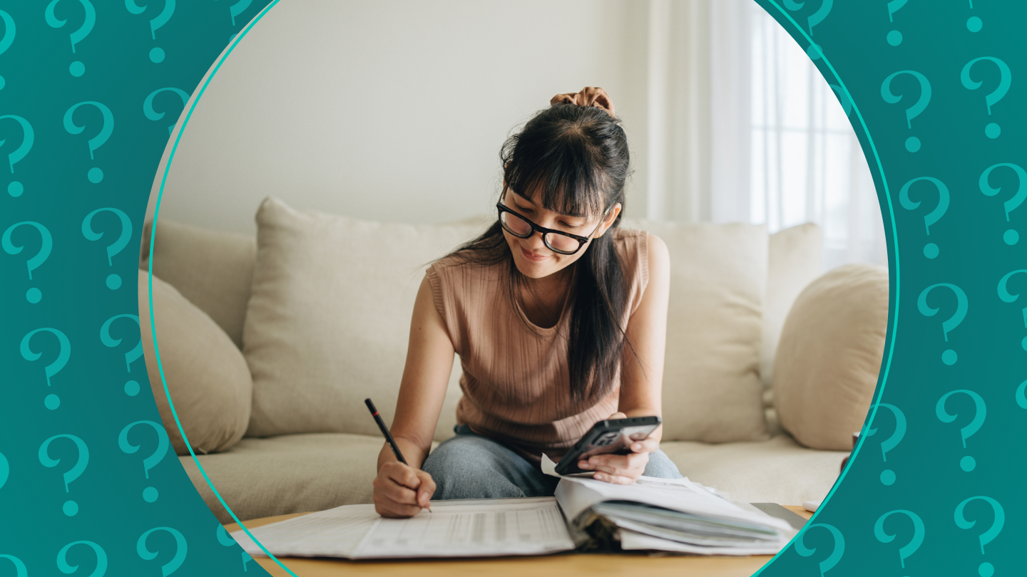 Woman sitting on a couch working a budget with pen and paper and a cell phone