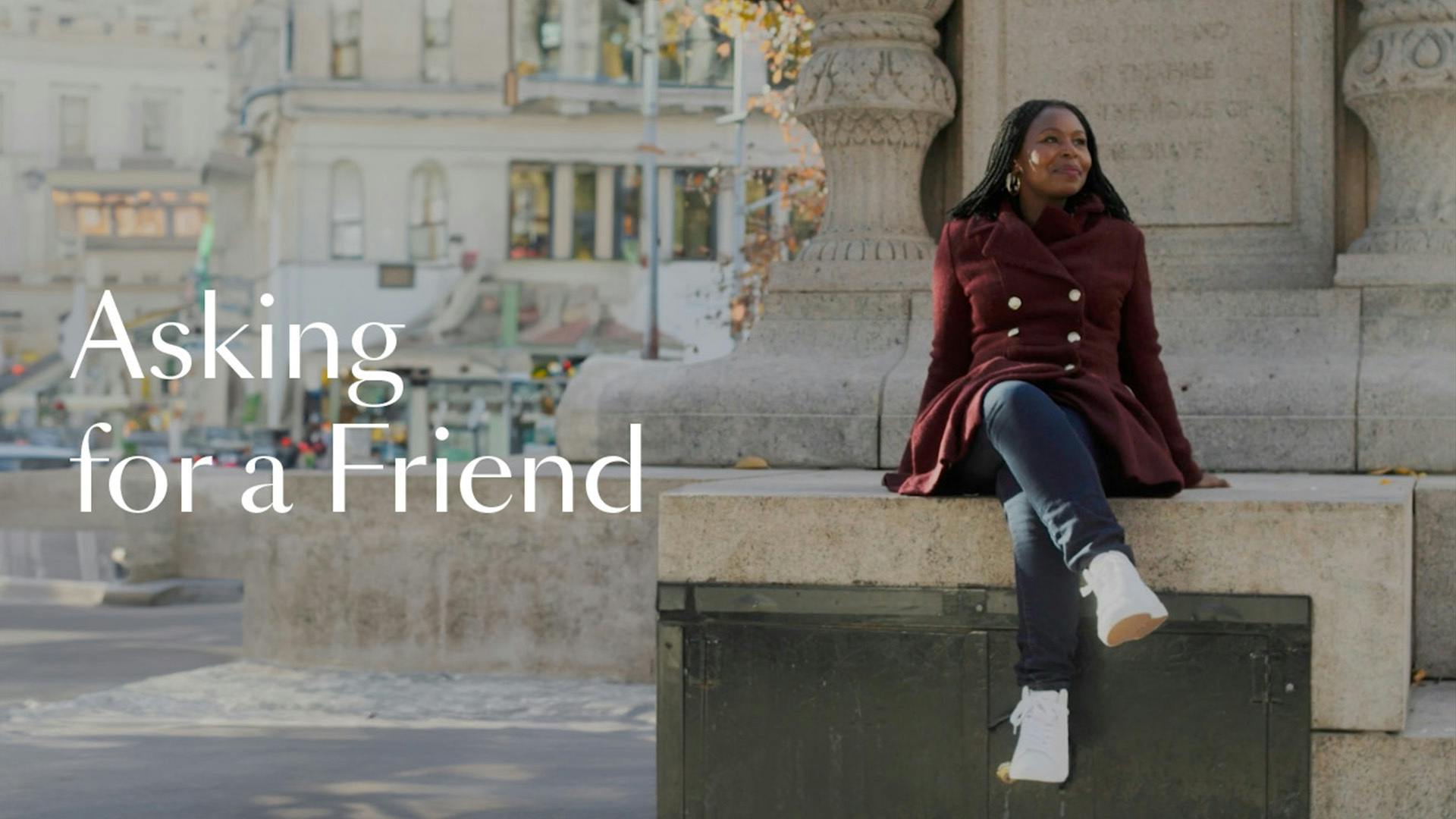 Kara Stevens sits on a statue in New York City wearing a burgundy coat, jeans, and high-top sneakers