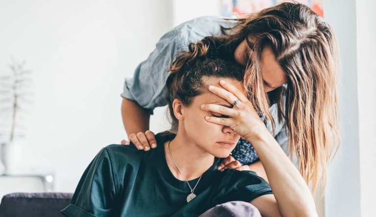One woman comforts another woman by kissing her on the forehead and putting an arm on her shoulder. The woman being comforted has her hand over her face. This photo is being used to promote an article on the topic