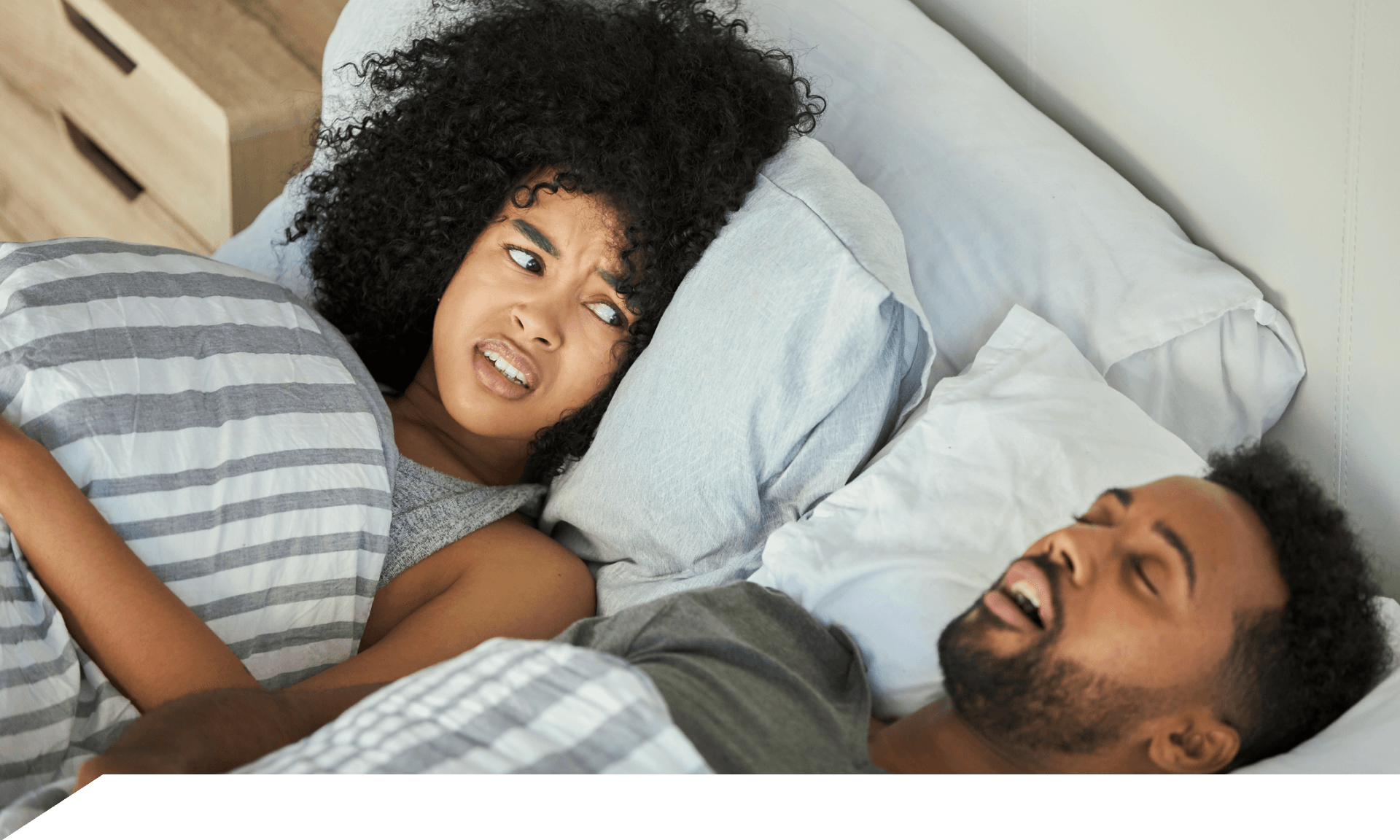A woman looking at her snoring male partner in bed