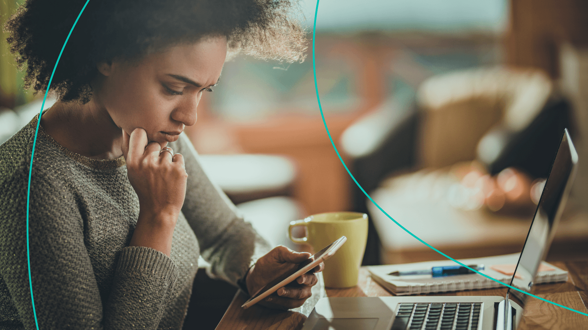 A woman looks at her phone while having her laptop open